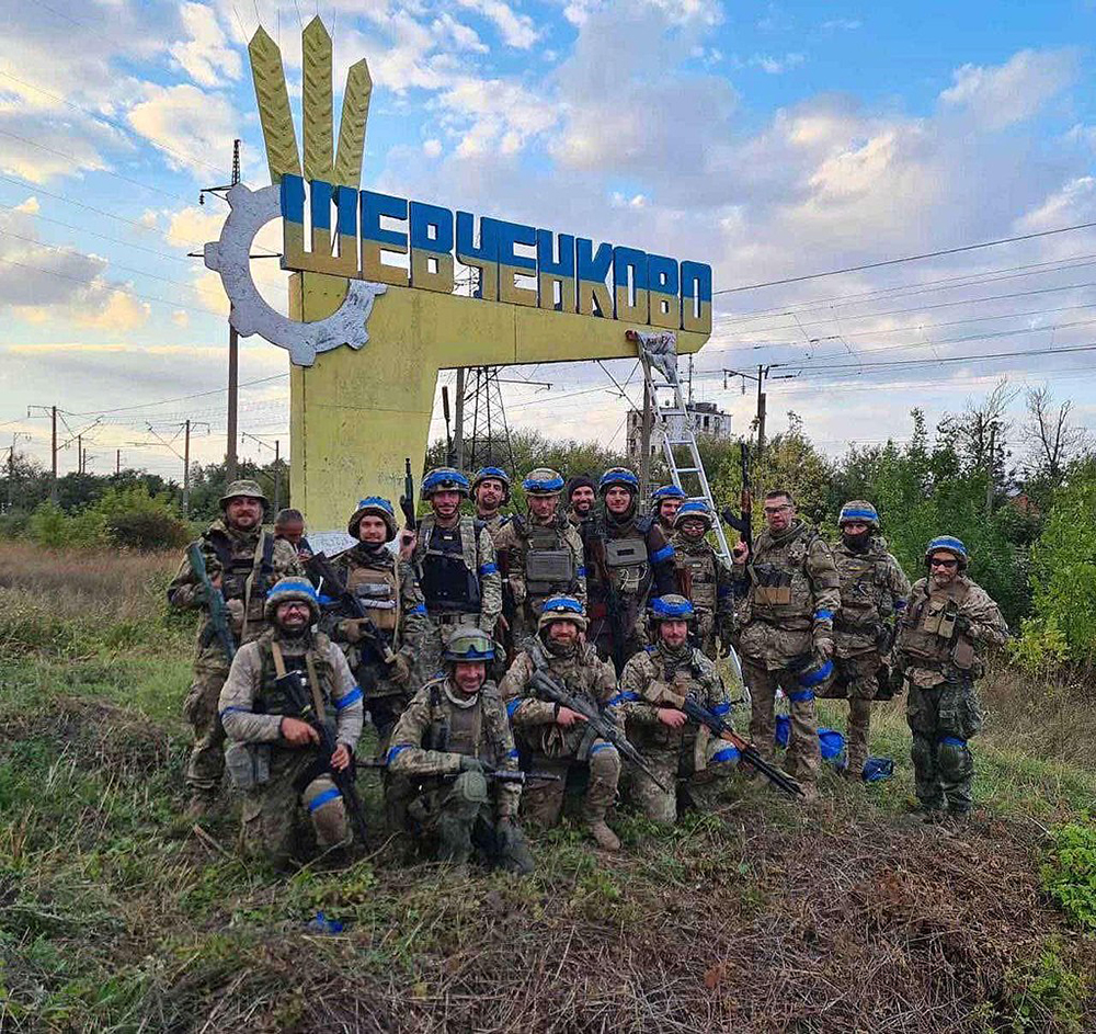 Key battles in Ukraine war: Ukrainian Territorial Defense soldiers pose near the entrance sign newly repainted to blue and yellow in the village of Shevchenkove, Kharkiv region, liberated from the Russian occupation in September 2022